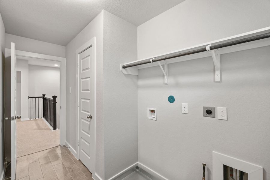 Located on the 2nd floor, a stylish laundry room where practicality meets a contemporary aesthetic. The dark finishes lend a sophisticated touch, creating a space that is both functional and visually appealing. Both electric and gas connections available. Sample photo of completed home with similar floor plan. As-built interior colors and selections may vary.
