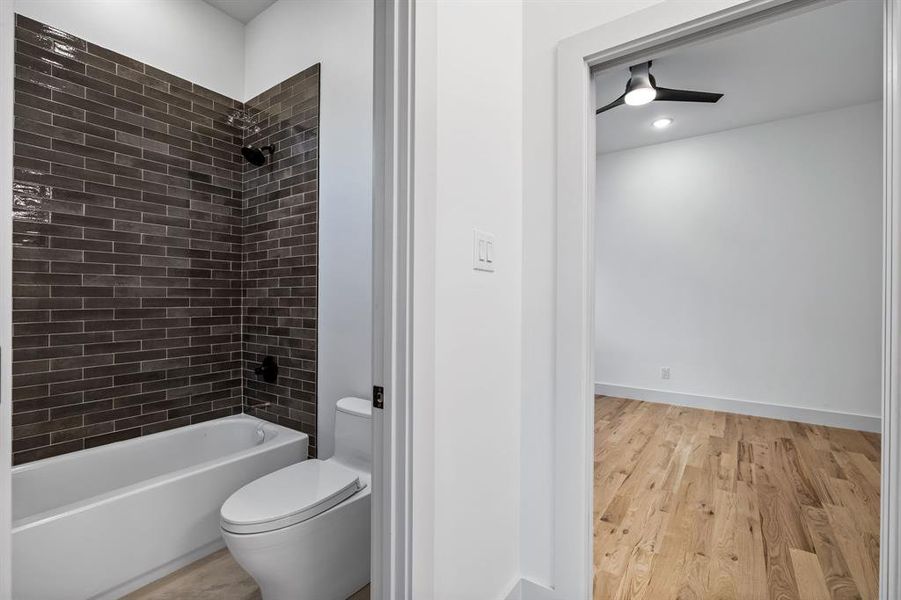 Bathroom featuring tiled shower / bath combo, ceiling fan, toilet, and wood-type flooring