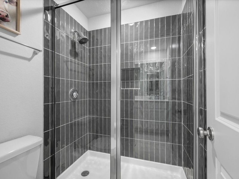 Floor to ceiling upgraded tile in shower with built-in niche, filtered shower head, glass enclosure