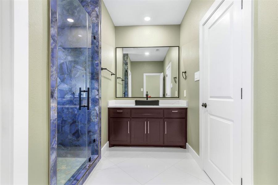 This modern bathroom features a striking blue-tiled shower with glass doors, a sleek vanity with a large mirror, and a clean, neutral color palette for a fresh, inviting look.