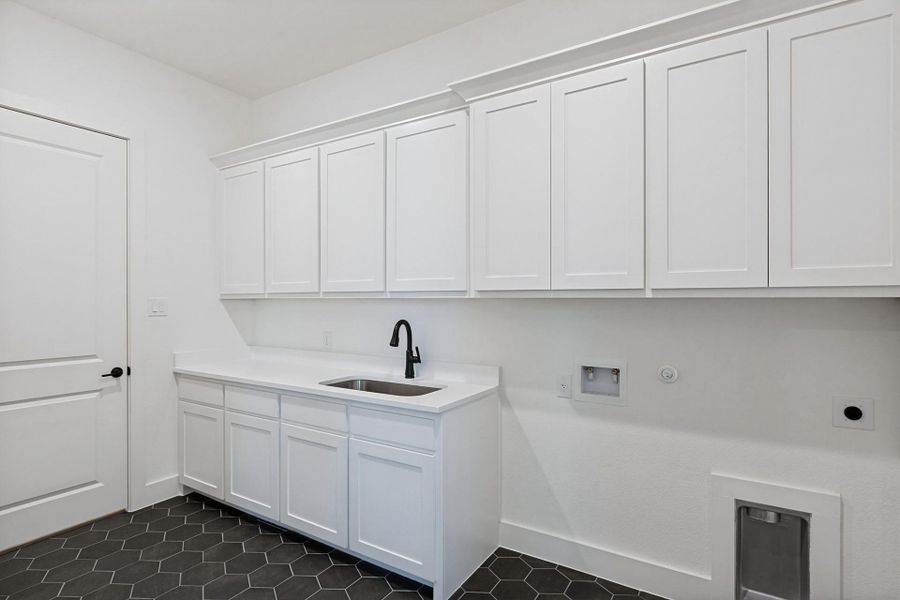 Abundant shaker cabinetry and dark hexagonal floor tiles define this functional utility space.