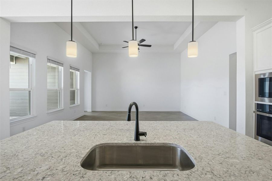 Kitchen with hanging light fixtures, a raised ceiling, light stone countertops, stainless steel appliances, and open floor plan