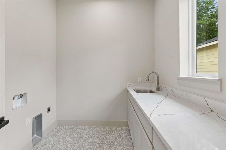 Dedicated laundry room featuring patterned floor tile, extensive countertop space with a single basin sink, a modern gooseneck faucet, and a large window. Dedicated laundry room featuring patterned floor tile, extensive countertop space with a single basin sink, a modern gooseneck faucet, and a large window.