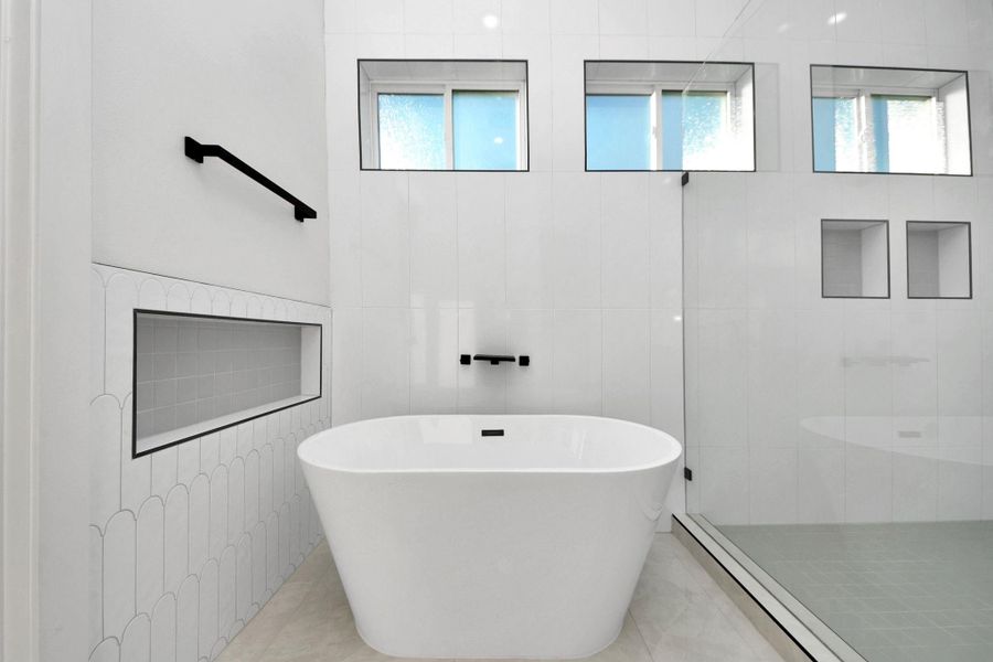 Unwind in the Woodbridge soaking tub beneath frosted windows that offer privacy and light. A custom-tiled nook beside the tub is perfect for your essentials, complemented by a waterfall faucet. Unwind in the Woodbridge soaking tub beneath frosted windows that offer privacy and light. A custom-tiled nook beside the tub is perfect for your essentials, complemented by a waterfall faucet.