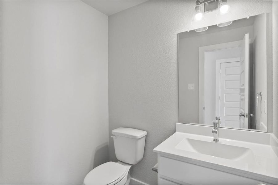 Sophisticated half bathroom adorned with contemporary finishes. The elegant 5-panel door welcomes you to a space where style meets functionality. Notice the sleek hardware accents that add a touch of modern charm. The vanity boasts light-colored countertops, beautifully complemented by a tasteful vanity light, creating a well-lit and inviting atmosphere. Sample photo of completed home with similar floor plan. As-built interior colors and selections may vary.