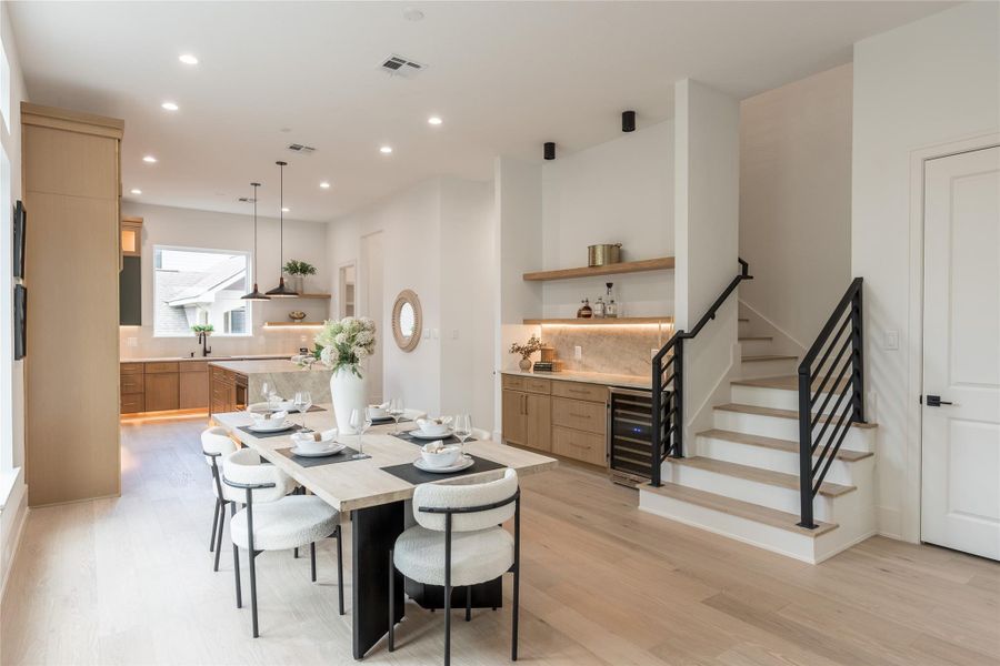 Three material gestures working in concert: the floor-to-ceiling oak pantry, the waterfall quartzite island crowned by a trio of dome pendants, and the open-tread staircase in matte-black steel. A kitchen composed like an architectural drawing: and it shows.