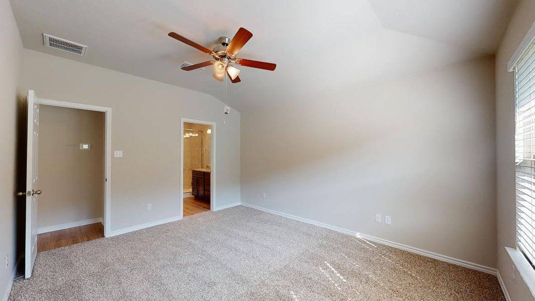 Unfurnished bedroom featuring light colored carpet, vaulted ceiling, a ceiling fan, and ensuite bathroom