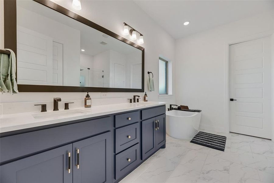 Full bathroom with a freestanding bath, a stall shower, double vanity, light marble finish floors, and recessed lighting