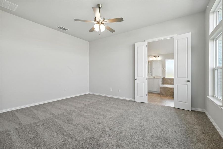 Unfurnished bedroom with carpet flooring, multiple windows, connected bathroom, and ceiling fan Unfurnished bedroom with carpet flooring, multiple windows, connected bathroom, and ceiling fan