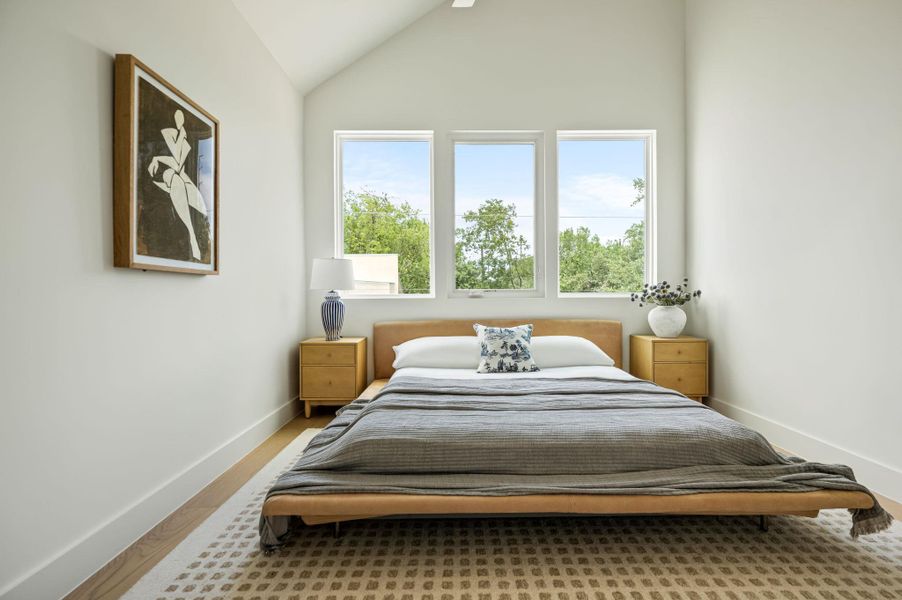 Sun-filled bedroom featuring a soaring vaulted ceiling and large windows overlooking lush greenery.