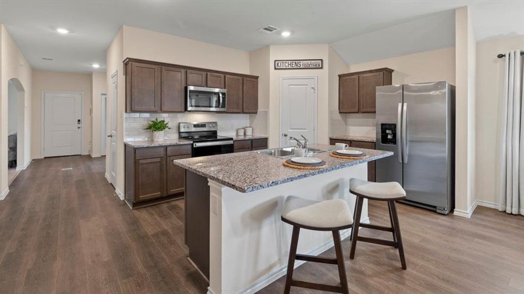Kitchen featuring stainless steel appliances, dark wood finish cabinets, a kitchen bar, a kitchen island with sink, and dark wood-type flooring