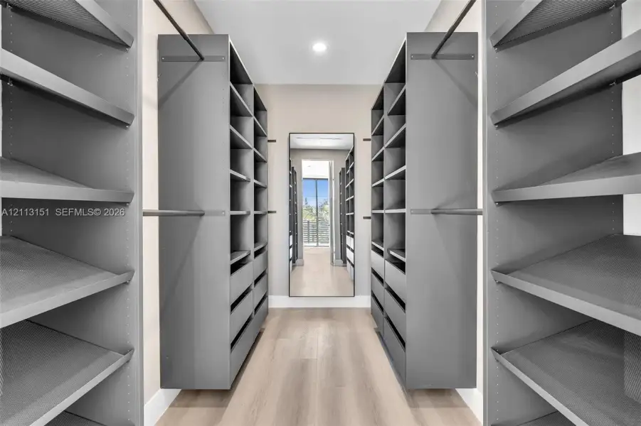 Custom walk-in storage featuring charcoal-finished built-in cabinetry, adjustable open shelving, integrated hanging rods, and wood-finish flooring Custom walk-in storage featuring charcoal-finished built-in cabinetry, adjustable open shelving, integrated hanging rods, and wood-finish flooring