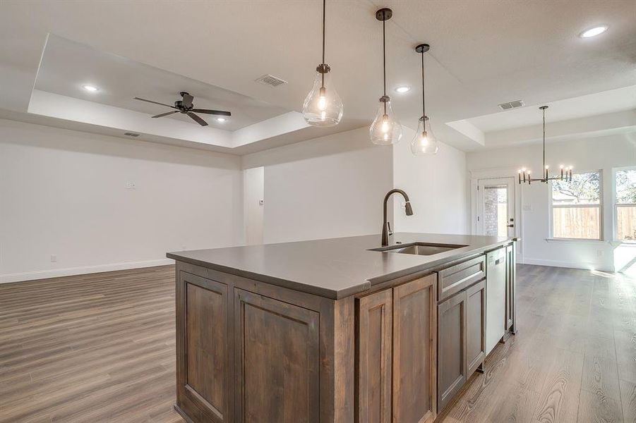 Kitchen with a raised ceiling, open floor plan, dark wood-type flooring, pendant lighting, and recessed lighting