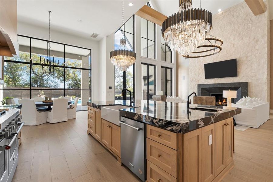 Kitchen featuring a lit fireplace, light brown cabinets, a center island with sink, light wood-type flooring, and recessed lighting