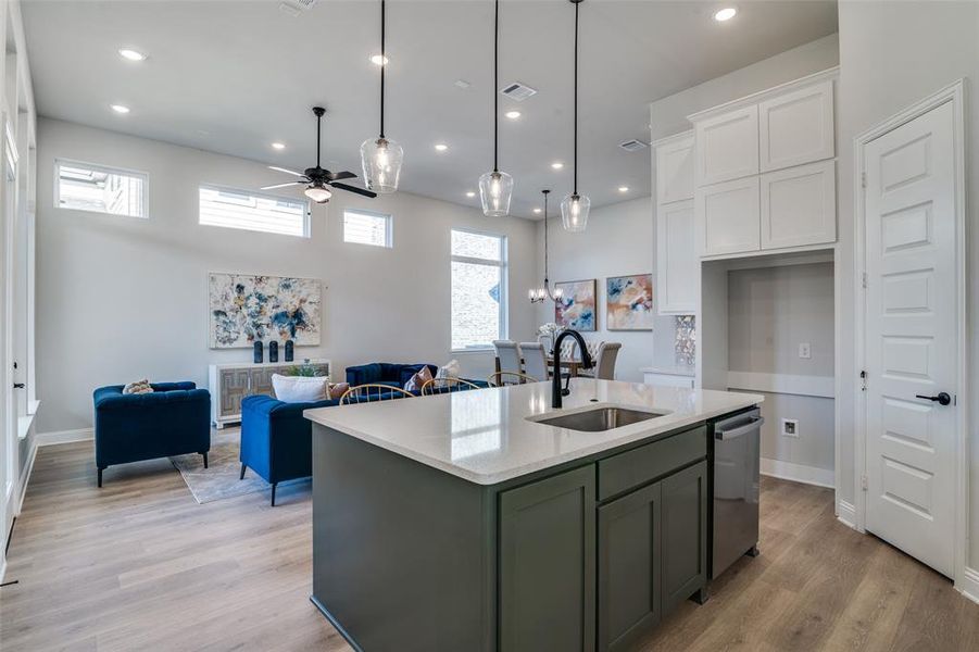 Kitchen with ceiling fan, sink, dishwasher, white cabinetry, and an island with sink