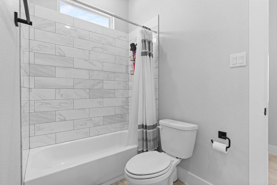 Bathroom featuring toilet and shower / bath combination with curtain