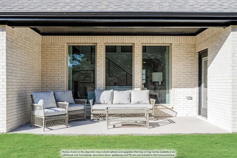 Covered back patio with wicker furniture set on concrete slab, brick exterior walls, and large sliding glass doors