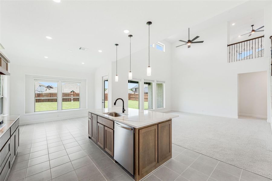 Open-concept kitchen with center island, pendant lights, and high ceilings opening to living area
