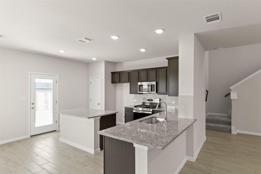 Kitchen with stainless steel appliances, light stone counters, a kitchen island, dark brown cabinetry, and light wood finished floors