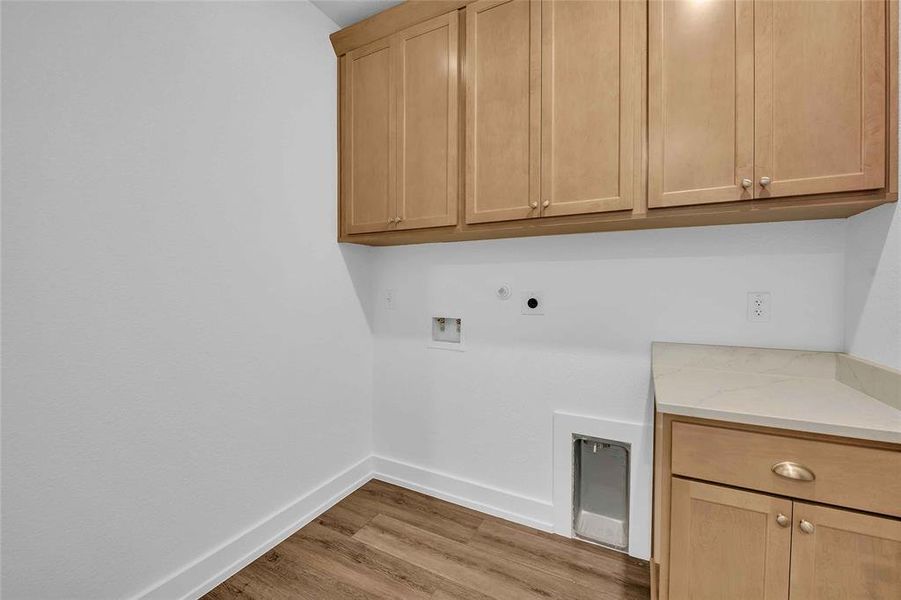Clothes washing area featuring baseboards, hookup for a washing machine, light wood-style floors, electric dryer hookup, and cabinet space Clothes washing area featuring baseboards, hookup for a washing machine, light wood-style floors, electric dryer hookup, and cabinet space