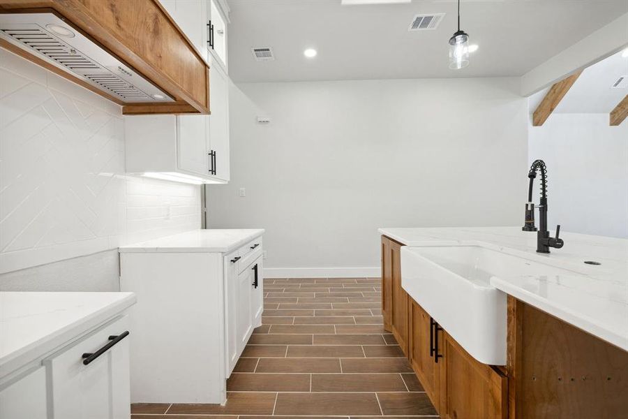 Kitchen featuring hanging light fixtures, light stone countertops, sink, and white cabinets