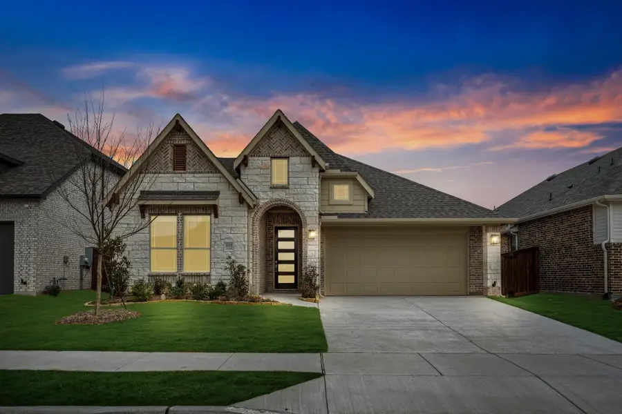 Two-story home with stone and brick exterior, two-car garage, arched entry, and green front lawn at dusk Two-story home with stone and brick exterior, two-car garage, arched entry, and green front lawn at dusk