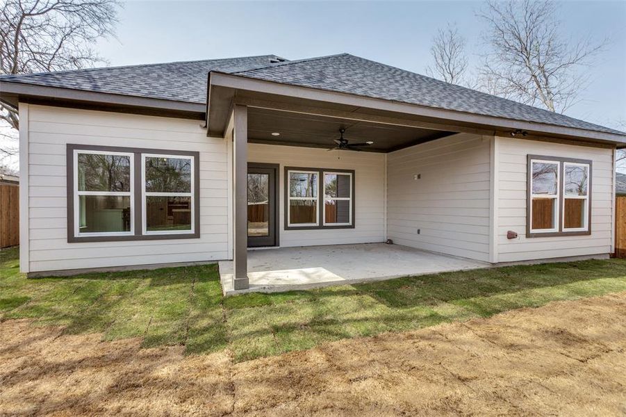 Back of property featuring ceiling fan, a yard, a shingled roof, and a patio area