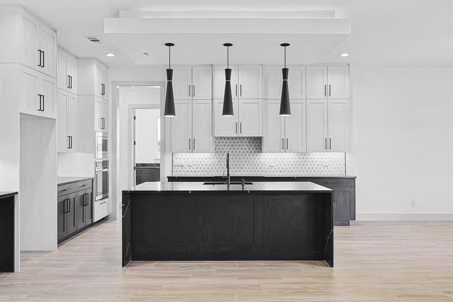 Kitchen featuring white cabinets, a center island with sink, sink, appliances with stainless steel finishes, and decorative light fixtures