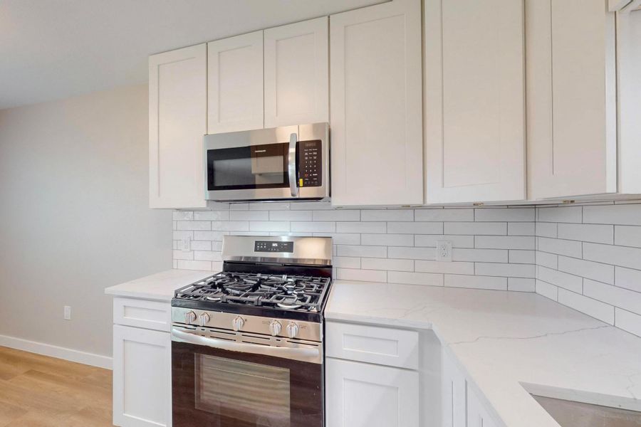 Kitchen with light wood-style floors, appliances with stainless steel finishes, baseboards, and white cabinetry