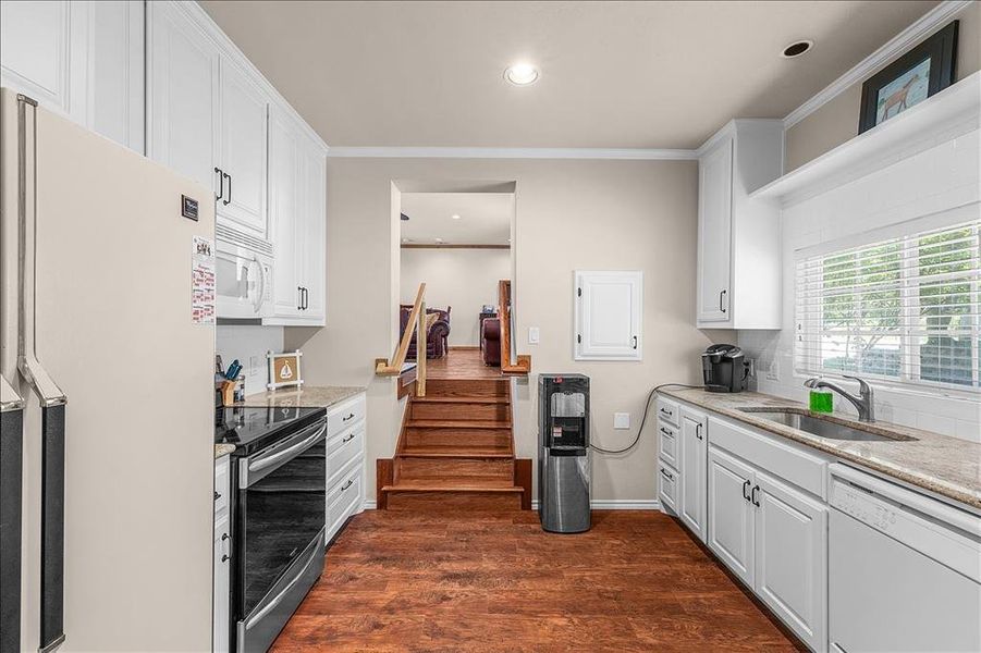 Kitchen featuring white appliances, white cabinets, dark wood finished floors, crown molding, and recessed lighting