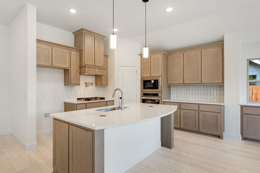 Kitchen with large center island, light wood cabinets, white countertops, and pendant lights above sink