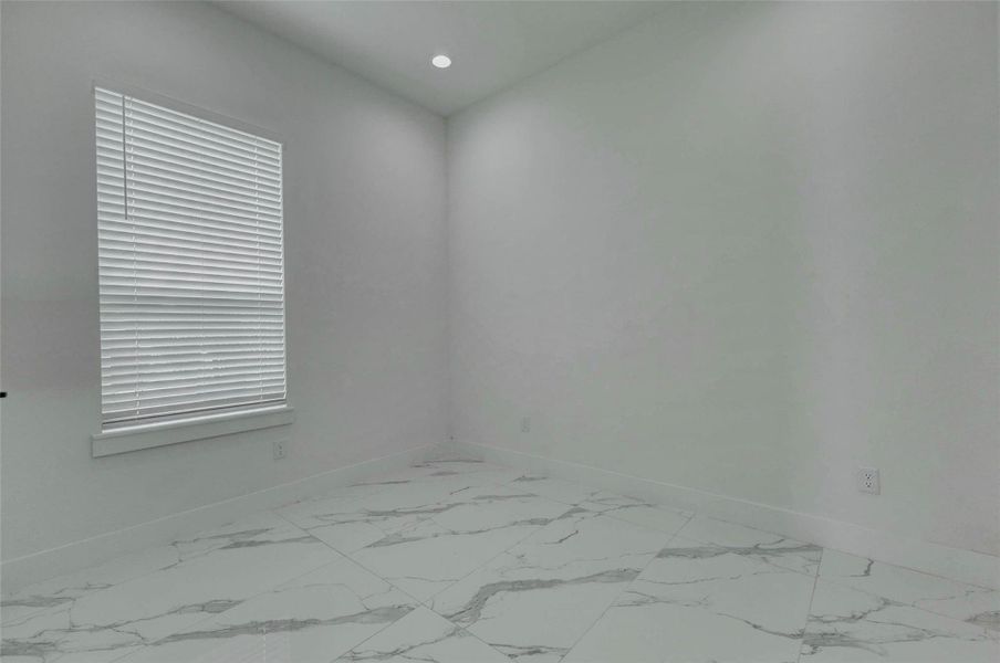 This bright first-floor bedroom offers a versatile setting with recessed lighting, neutral walls, window blinds, and glossy marble-look tile flooring. The flexible footprint can accommodate bedroom furniture, a desk, exercise equipment, or creative workspace.