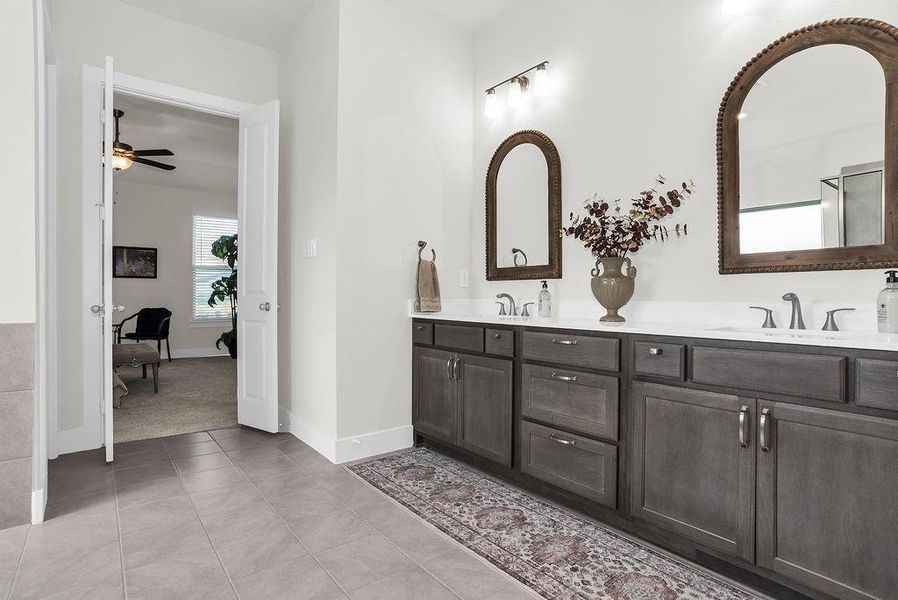 Main ensuite bath features dual vanity with wood-finish cabinetry, brush bronze faucets,  glass-enclosed steam shower with a tiled surround and vertical accent, a freestanding soaking tub ceramic tile floors and spacious walk-in closet with built-in shelving.