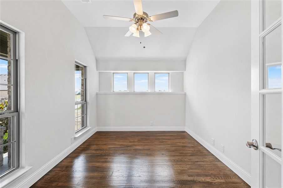 Empty room with vaulted ceiling, dark wood-style floors, and a ceiling fan Empty room with vaulted ceiling, dark wood-style floors, and a ceiling fan
