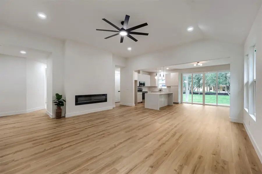 Open-concept interior featuring wood-finish flooring, an electric fireplace, and vaulted ceilings with recessed lighting