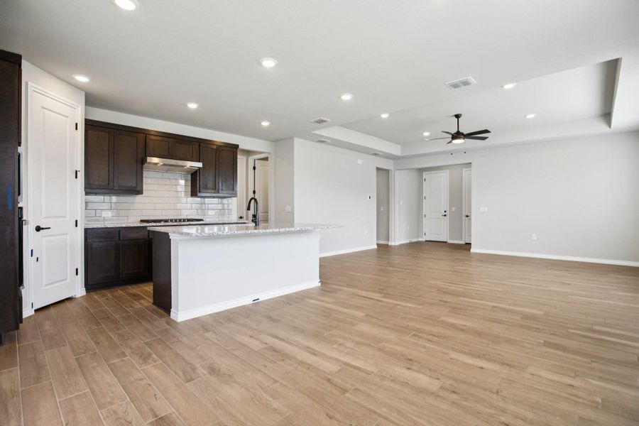 Kitchen featuring backsplash, recessed lighting, light stone countertops, a kitchen island with sink, and a tray ceiling Kitchen featuring backsplash, recessed lighting, light stone countertops, a kitchen island with sink, and a tray ceiling