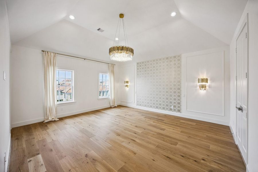 Spacious primary suite with hardwood floors, designer lighting and abundant natural light.  Designer wallpaper on the headboard wall, elegant wall sconces, and custom millwork add sophisticated architectural detail.