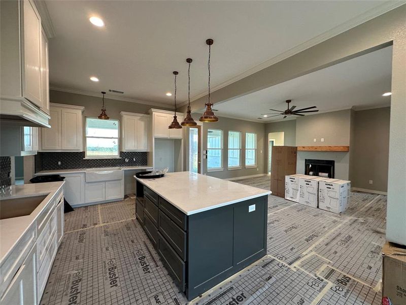 Kitchen with ceiling fan, a center island, hanging light fixtures, backsplash, and white cabinets