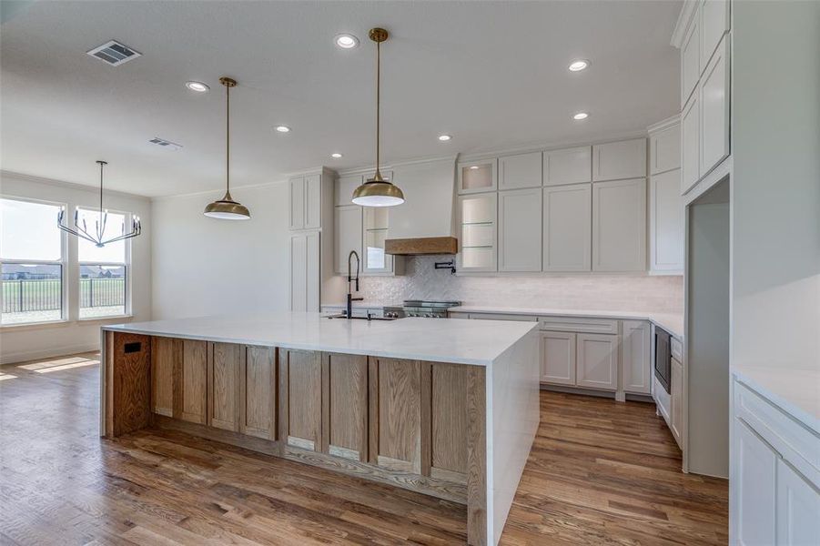 Kitchen featuring decorative backsplash, an island with sink, white cabinets, wood-type flooring, and crown molding