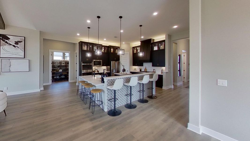 Kitchen with a kitchen bar, decorative light fixtures, a large island with sink, light wood-style flooring, and dark wood finish cabinetry