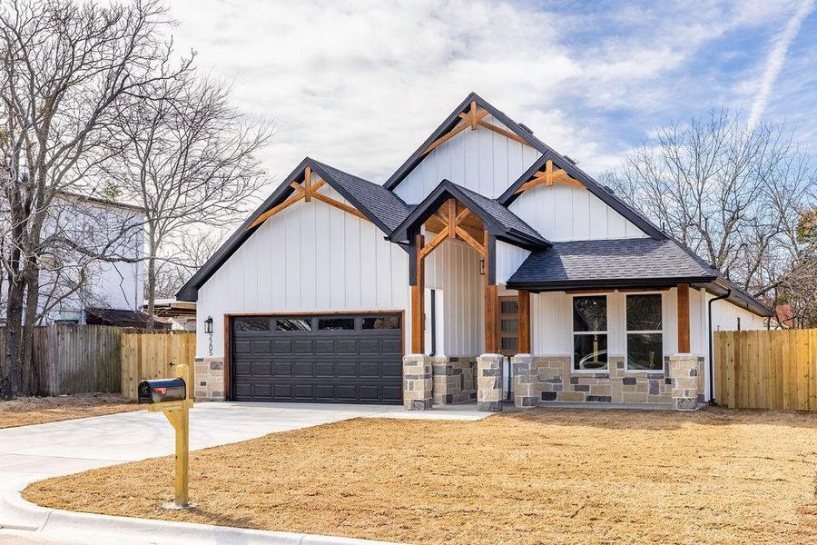 Modern farmhouse with an attached garage, fence, concrete driveway, and roof with shingles