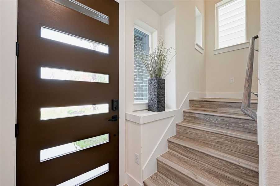 This photo showcases a modern entryway with a sleek wooden door featuring horizontal glass inserts, providing natural light. The adjacent staircase has stylish vinyl flooring.