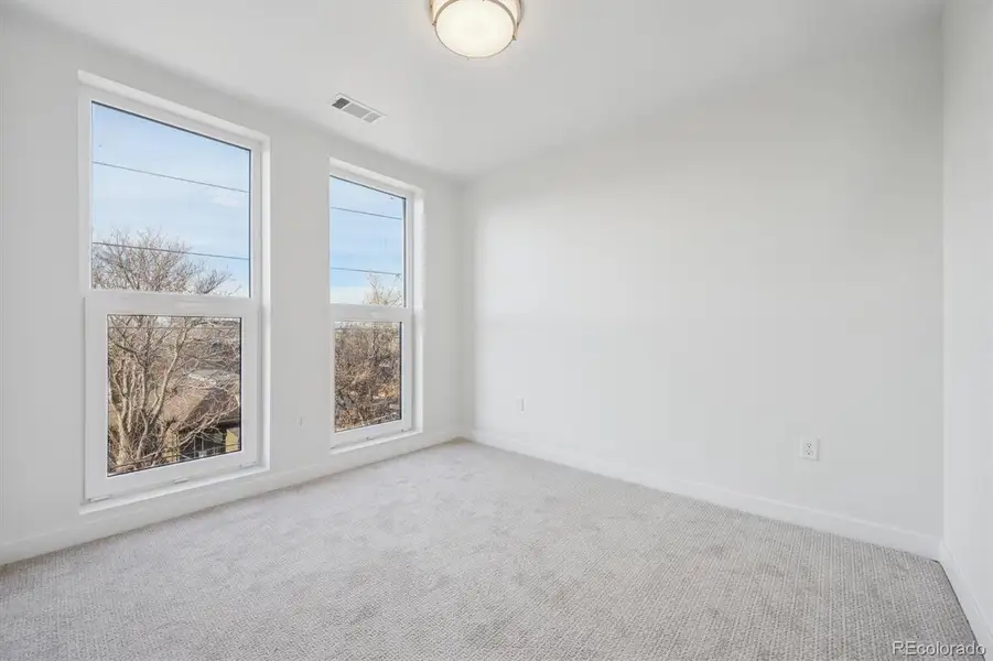 Light-filled primary bedroom with plush carpeting, large windows, and generous closet space.