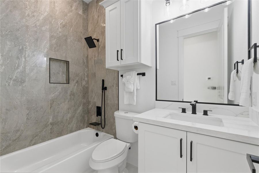 This hall bathroom features ample storage, a shower-tub combo with a built-in soap niche, and contemporary fixtures for a clean, modern look.