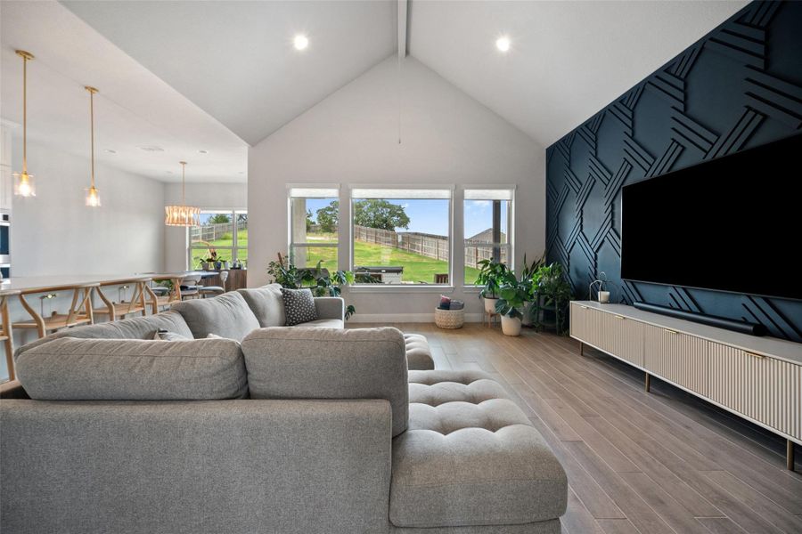 Living area with wood finished floors, an accent wall, and high vaulted ceiling