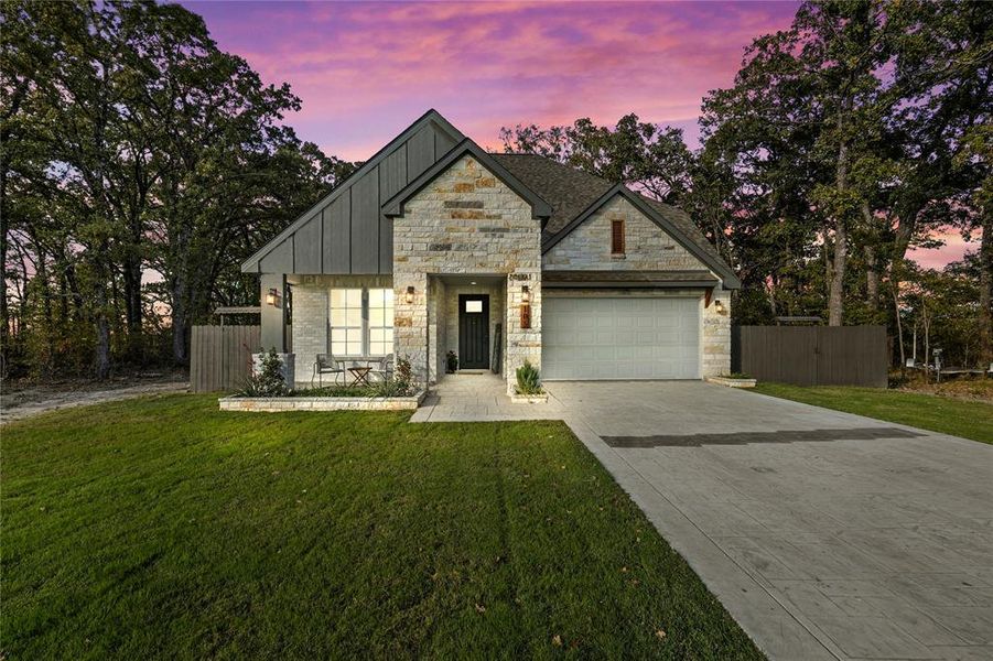 View of front facade featuring driveway, stone siding, an attached garage, and board and batten siding
