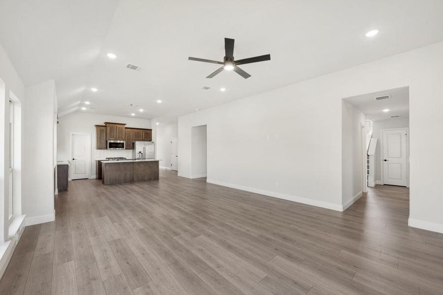 Open living area with hardwood floors and ceiling fan, open to kitchen with dark cabinets and island Open living area with hardwood floors and ceiling fan, open to kitchen with dark cabinets and island
