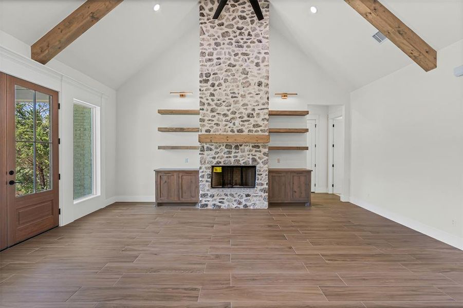 Unfurnished living room featuring beamed ceiling, wood tiled floors, a fireplace, high vaulted ceiling, and a ceiling fan Unfurnished living room featuring beamed ceiling, wood tiled floors, a fireplace, high vaulted ceiling, and a ceiling fan