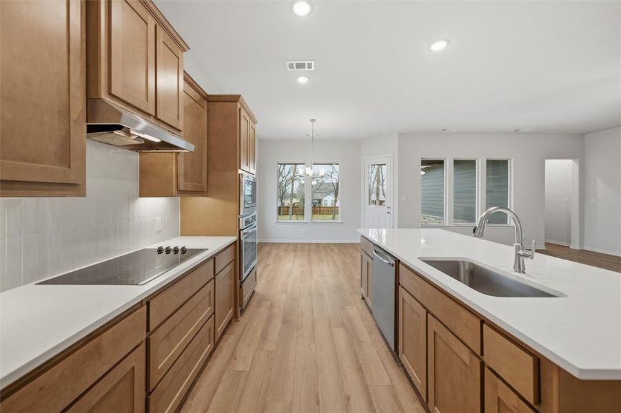 Kitchen featuring wood finish cabinets, light wood-style flooring, stainless steel appliances, tasteful backsplash, and light stone countertops Kitchen featuring wood finish cabinets, light wood-style flooring, stainless steel appliances, tasteful backsplash, and light stone countertops