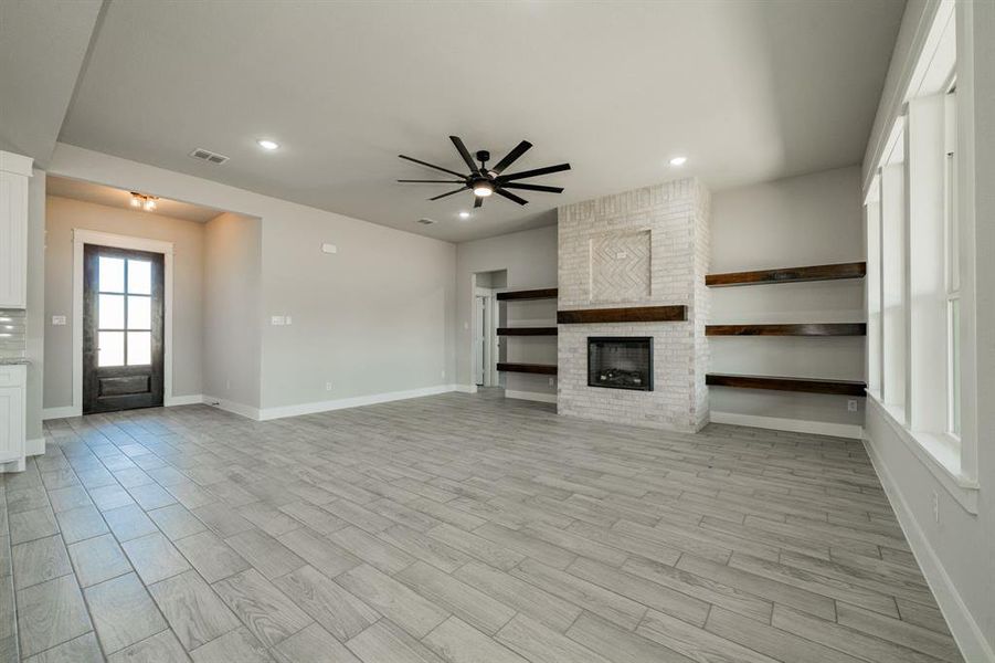 Living room featuring light wood-style flooring, electric fireplace, recessed lighting, ceiling fan and floating shelves Living room featuring light wood-style flooring, electric fireplace, recessed lighting, ceiling fan and floating shelves